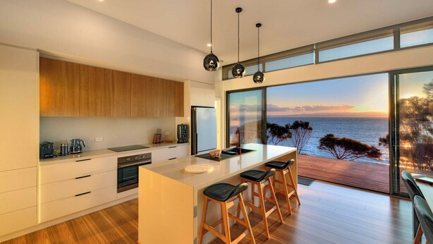 A modern kitchen with a large island, wooden cabinets, and a view of the sea. - Freycinet Coastal Retreat - Freycinet Holiday Houses (Coles Bay)