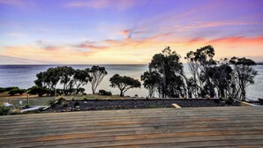 A wooden deck with a view of the sea and trees at sunset. - Freycinet Coastal Retreat - Freycinet Holiday Houses (Coles Bay)