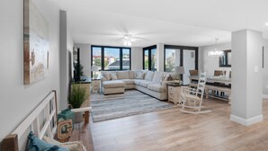 Ein geräumiges Wohnzimmer mit einer Eckcouch, einem Essbereich mit Tisch und Stühlen und großen Fenstern mit Blick nach draußen.