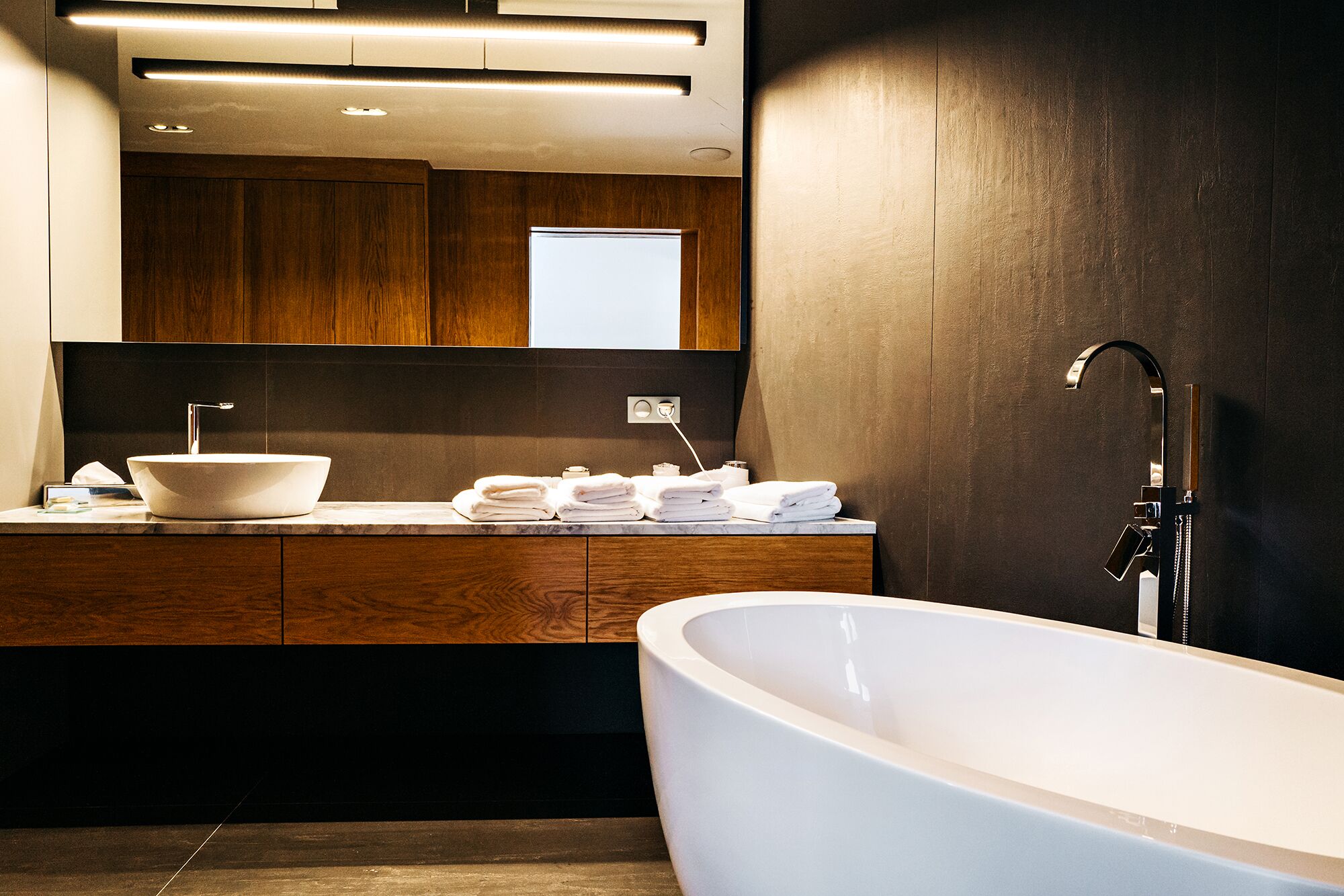 Un baño moderno con una bañera independiente, un lavamanos grande con lavabo a la vista y un mueble de tocador de madera con espejo.