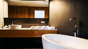 Un baño moderno con una bañera independiente, un lavamanos grande con lavabo a la vista y un mueble de tocador de madera con espejo.