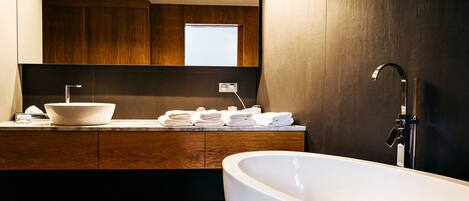 A modern bathroom with a freestanding bathtub, a large sink with a vessel basin, and a wooden vanity with a mirror above.