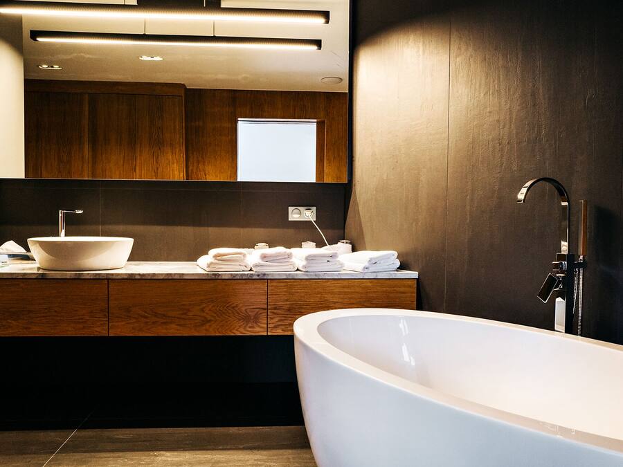 Un baño moderno con una bañera independiente, un lavamanos grande con lavabo a la vista y un mueble de tocador de madera con espejo.