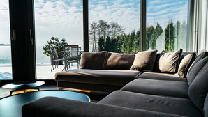 A modern living room with a large window, a sofa, and a dining area with chairs and a table. - Przystań Hotel & Restaurants (Olsztyn)