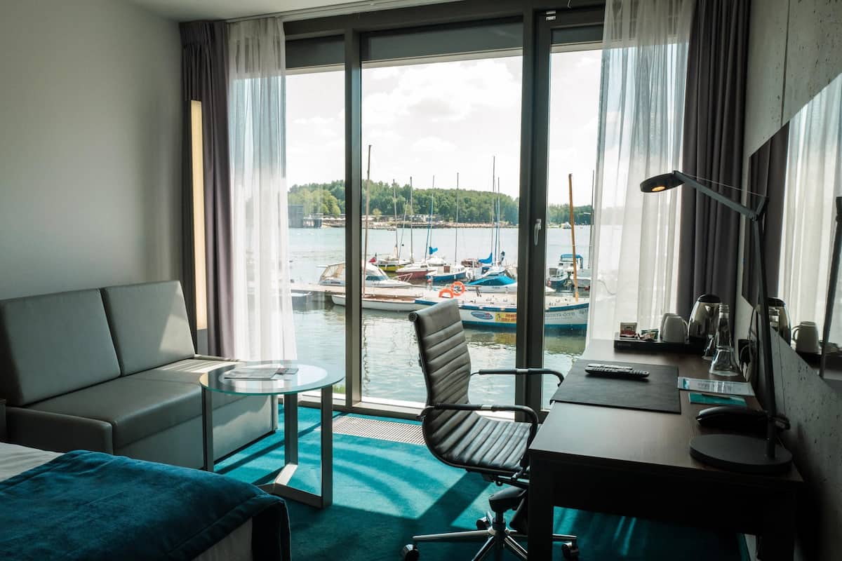 A hotel room with a view of boats on a lake, a desk with a computer, a chair, and a sofa.