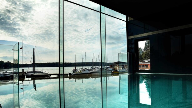 A clear indoor swimming pool with a view of sailboats docked at a marina. - Przystań Hotel & Restaurants (Olsztyn)