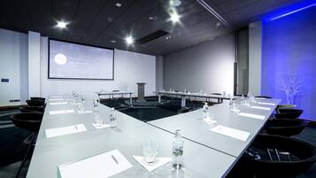 Une salle de conférence avec une longue table, des chaises, un écran de projection et un mur éclairé en bleu.