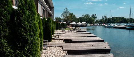 A waterfront dock area with wooden platforms, a row of umbrellas, and boats in the background.