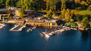 An aerial view of a marina with boats docked, a modern building with large windows, and a dock extending into the water. - Przystań Hotel & Restaurants (Olsztyn)