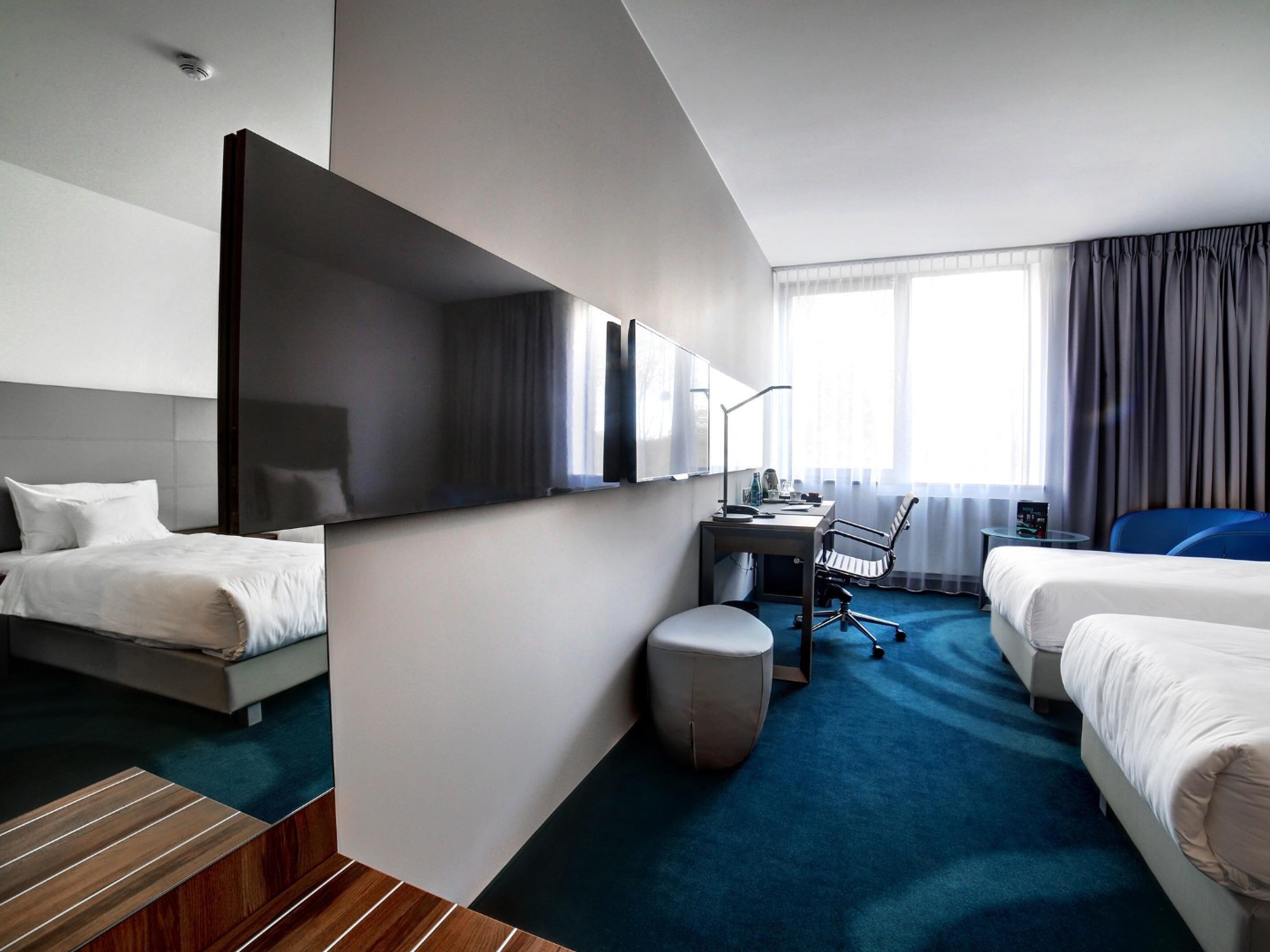 Hotelkamer met twee bedden, een bureau, een stoel, een tafeltje en een grote spiegel.