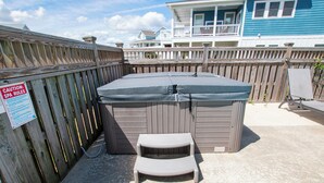 A hot tub with a wooden deck and a caution sign, a small step stool, and a pool table in a backyard.