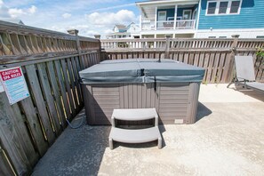 A hot tub with a wooden deck and a caution sign, a small step stool, and a pool table in a backyard.