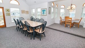A dining area with a large table and chairs, a smaller table with chairs, and a chandelier.