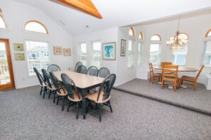 A dining area with a large table and chairs, a smaller table with chairs, and a chandelier.