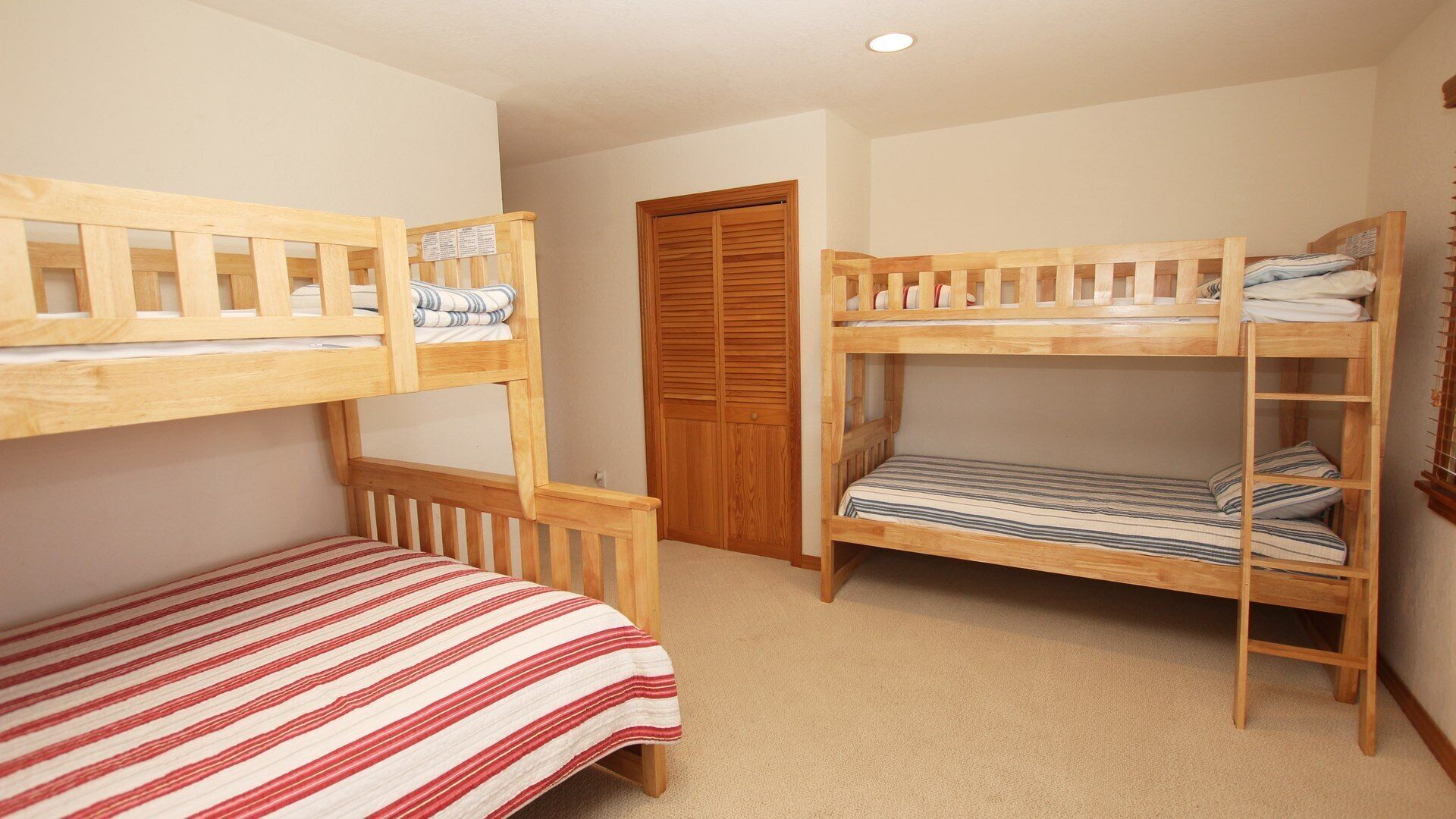 Een kamer met twee stapelbedden, een houten garderobe en een vloerbedekking.