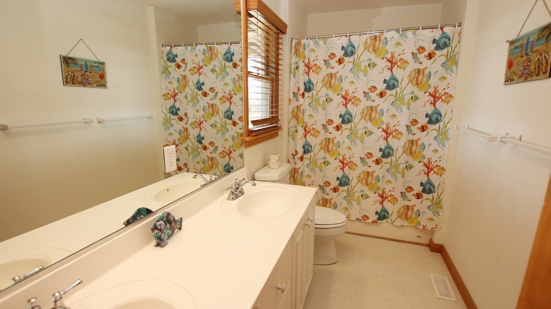 A bathroom with a white sink, mirror, and bathtub. There is a shower curtain with a fish pattern.