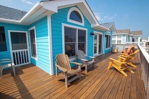Una casa azul con terraza de madera, dos sillas Adirondack y una pequeña mesa.