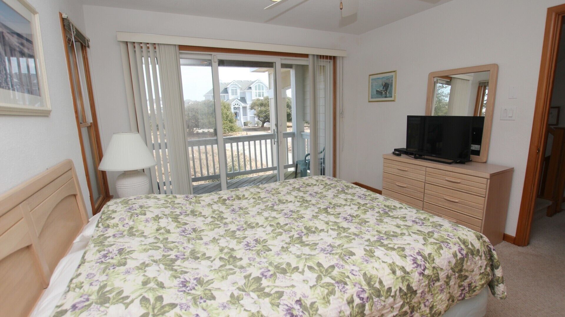 A bedroom with a bed, a dresser, a television, and a sliding glass door leading to an outdoor area.