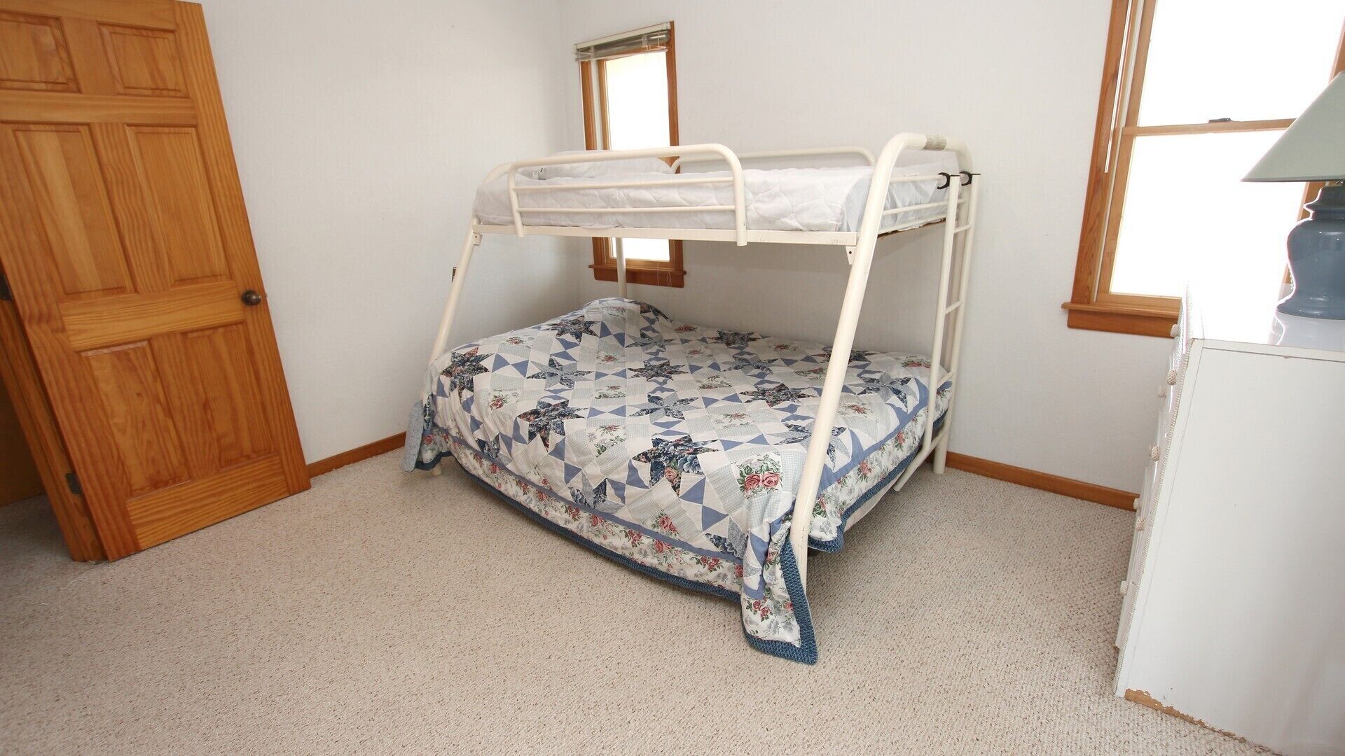 A bunk bed with a floral-patterned mattress in a room with a wooden door, a small window, and a white dresser.