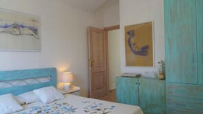 Een slaapkamer met een bed, een bedlamp, een houten deur, een blauwgroene kast en twee schilderijen aan de muur.