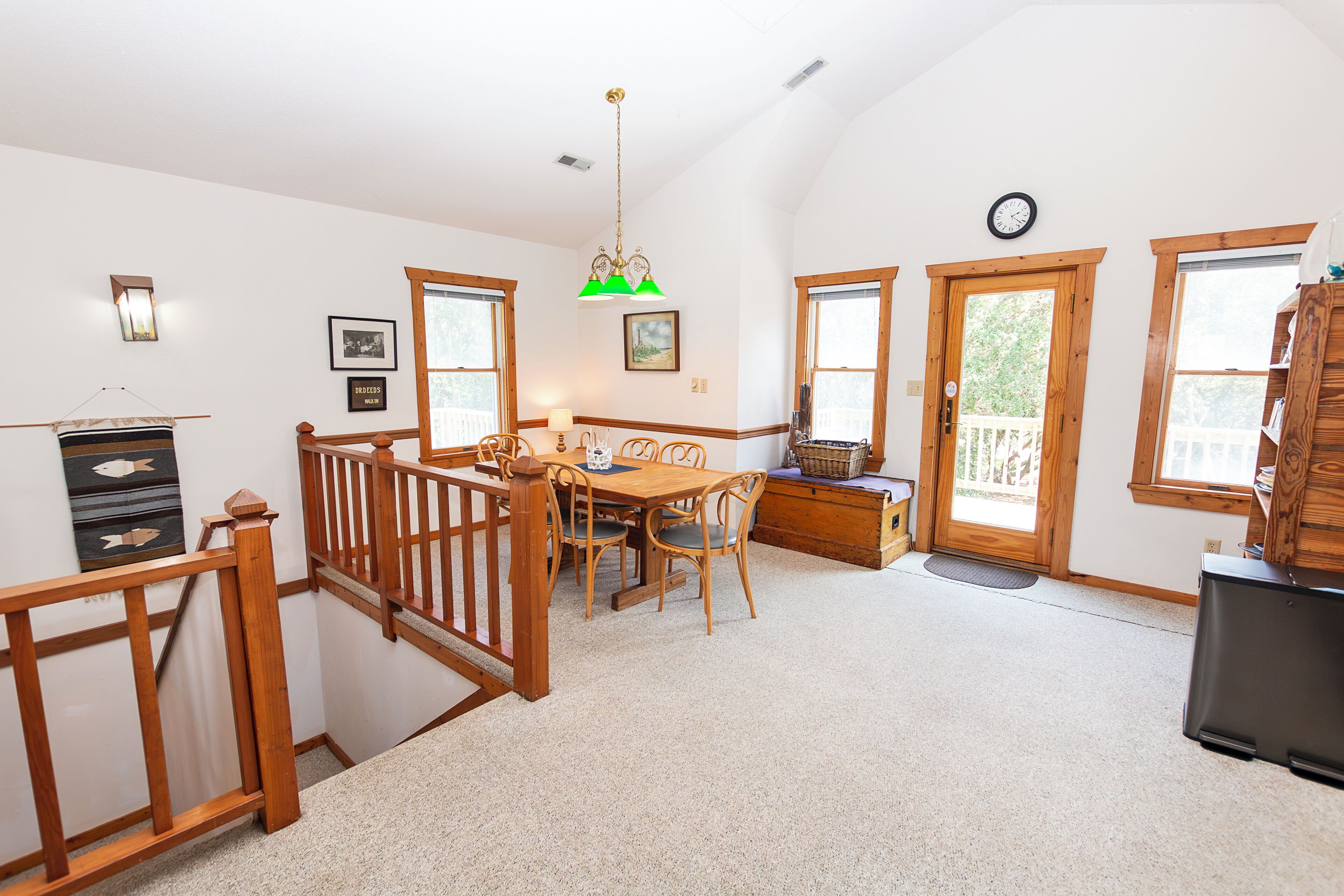 A dining area with a wooden table and chairs, a chandelier, and a view of the outdoors through large windows.