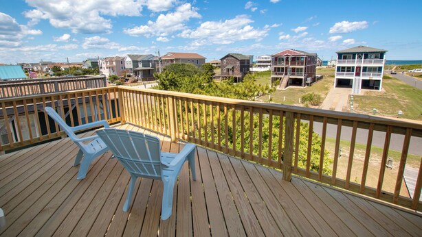 A wooden deck with two chairs, overlooking a residential area with houses and a beach. - Oceanside, Private Pool, Close to Beach Access and Shopping! KH1, Marabel-by-the-Sea (Kitty Hawk)