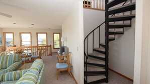 A living room with a spiral staircase, a dining area with wooden furniture, and large windows. - Oceanside, Community Pool, Community Tennis, PT7, Summer Winds (Duck)