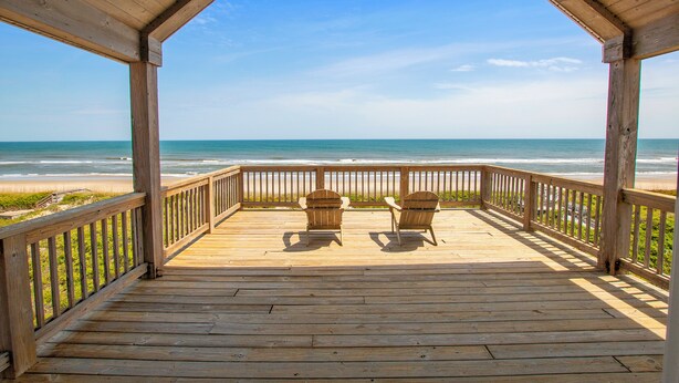 Un pontile di legno con due poltrone Adirondack rivolte verso la spiaggia.