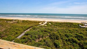 Una spiaggia con una passerella in legno, dune erbose e una vista aperta sull'oceano.
