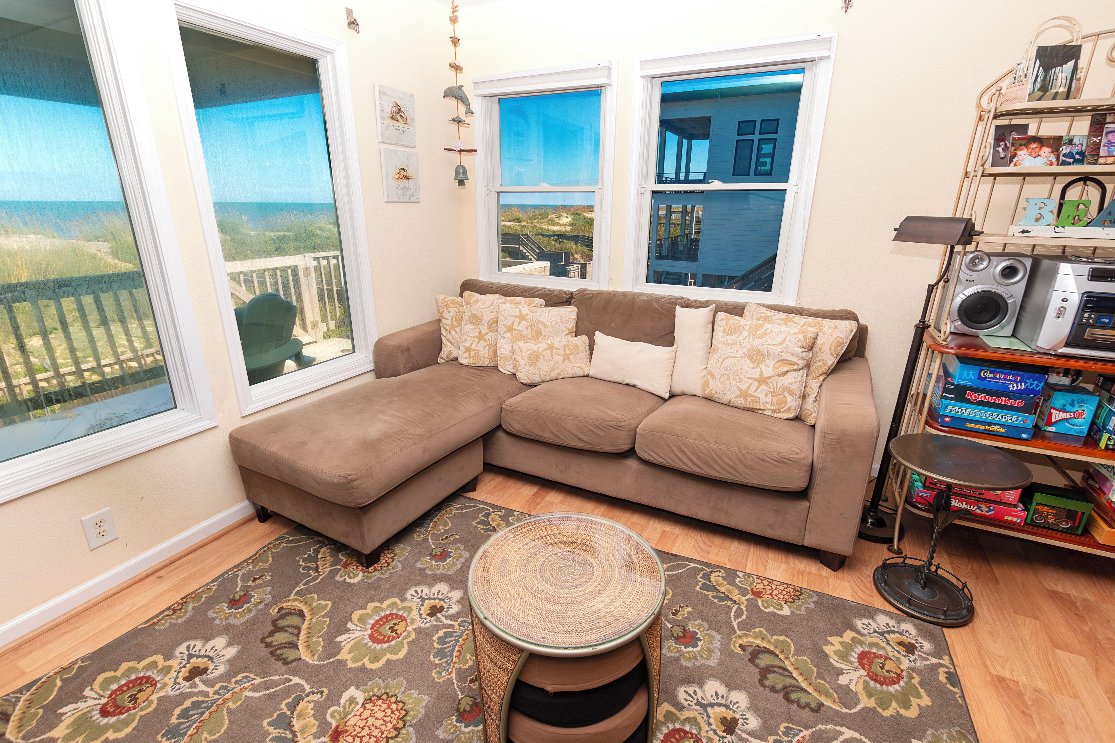 A living room with a large sectional sofa, a round coffee table, and a view of the beach through the windows.