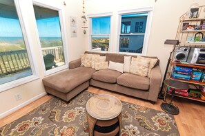 A living room with a large sectional sofa, a round coffee table, and a view of the beach through the windows.
