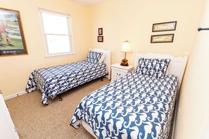 Un dormitorio con dos camas individuales, una mesita de noche, una lámpara y una ventana.