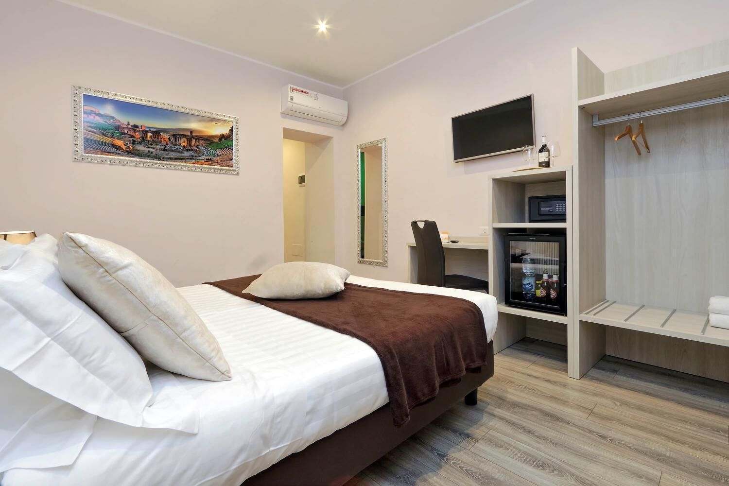 Habitación de hotel moderna con cama, televisor, refrigerador pequeño y armario.