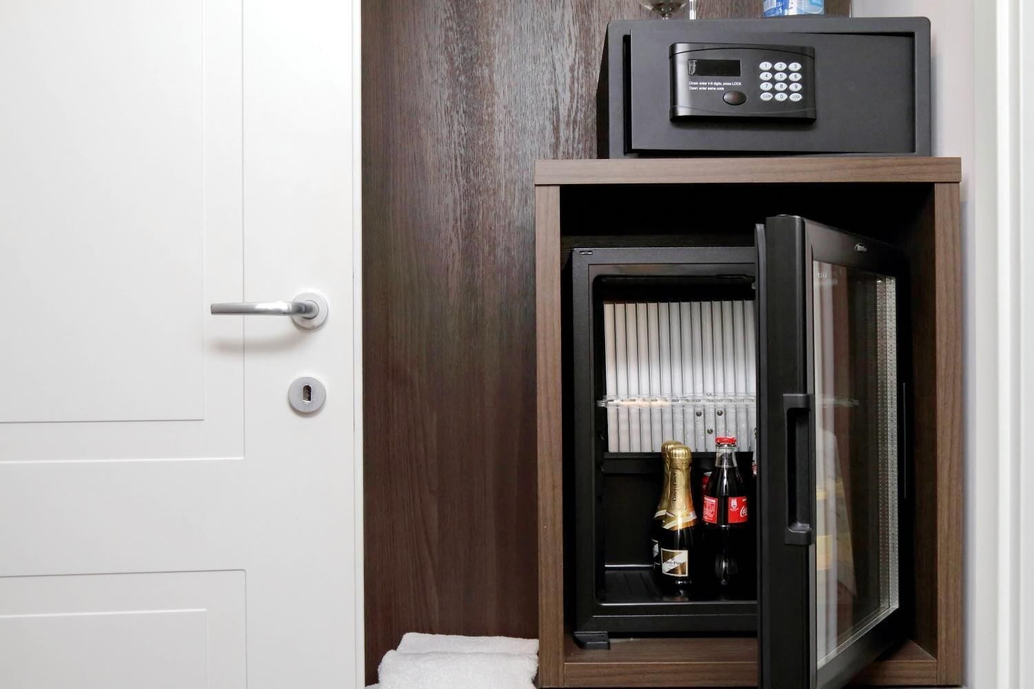A secure minibar with a digital lock, a bottle of champagne, and a bottle of Coca-Cola.