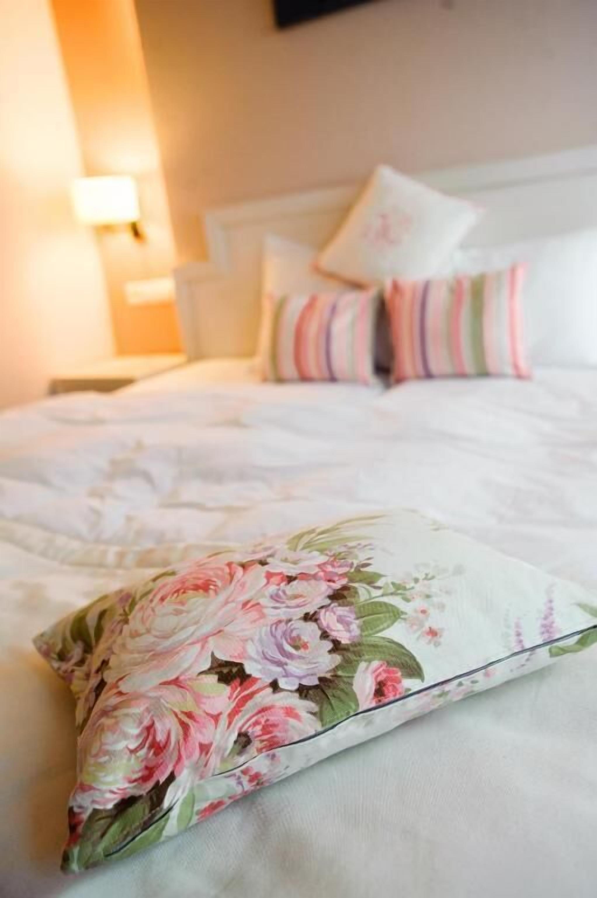 Una cama bien hecha con almohadas estampadas con flores y una colcha blanca.