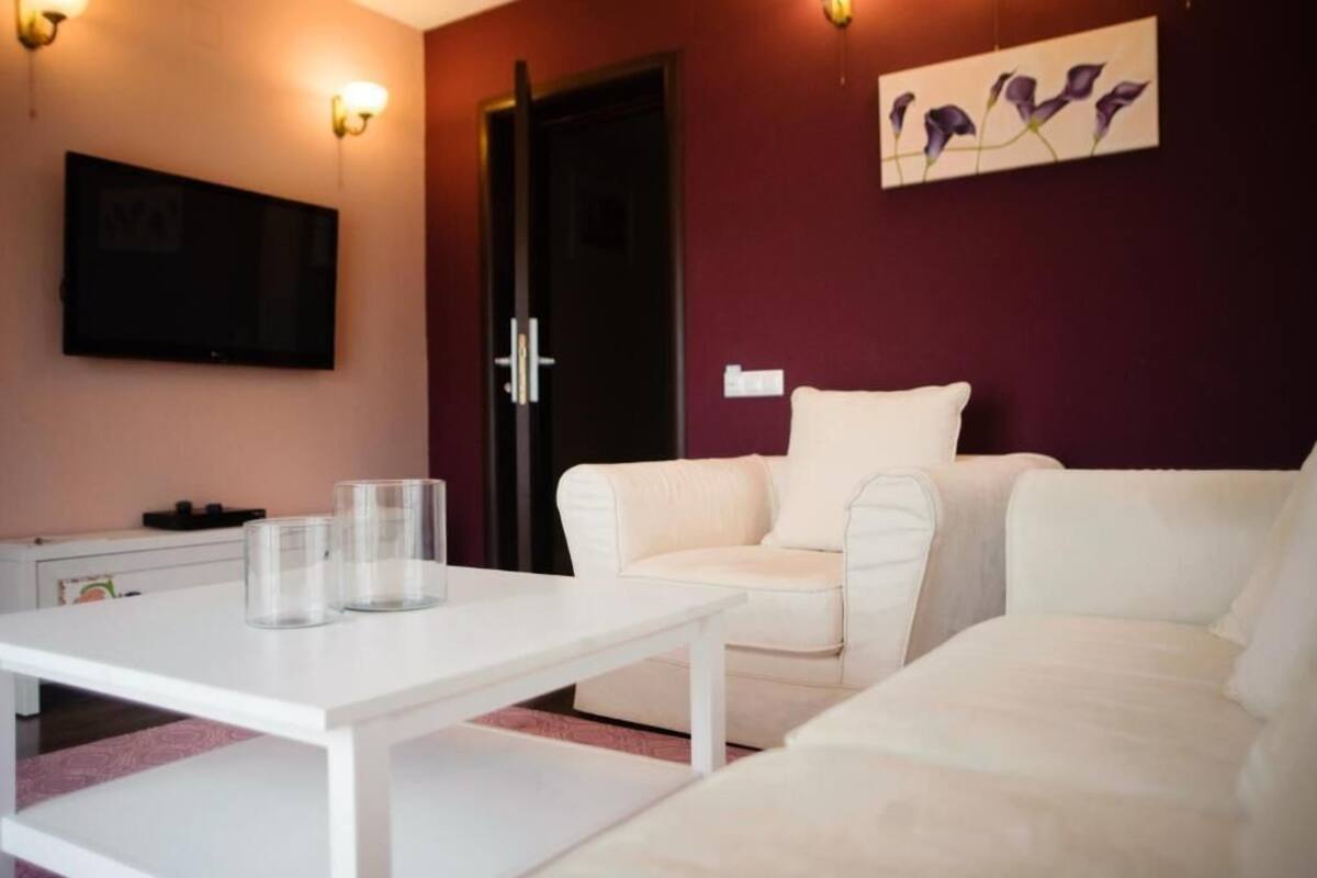 A living room with a white sofa, a white coffee table, and a flat-screen TV mounted on the wall.