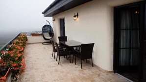 Een terras buiten met een tafel en stoelen, een hangstoel en een decoratieve vogelkooi.
