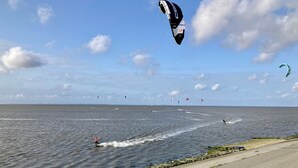 A coastal road with a view of the sea and multiple kitesurfers in the distance. - 5 Pers - Equipped House Gudrun With Sauna - Dogs are Welcome (Anjum)
