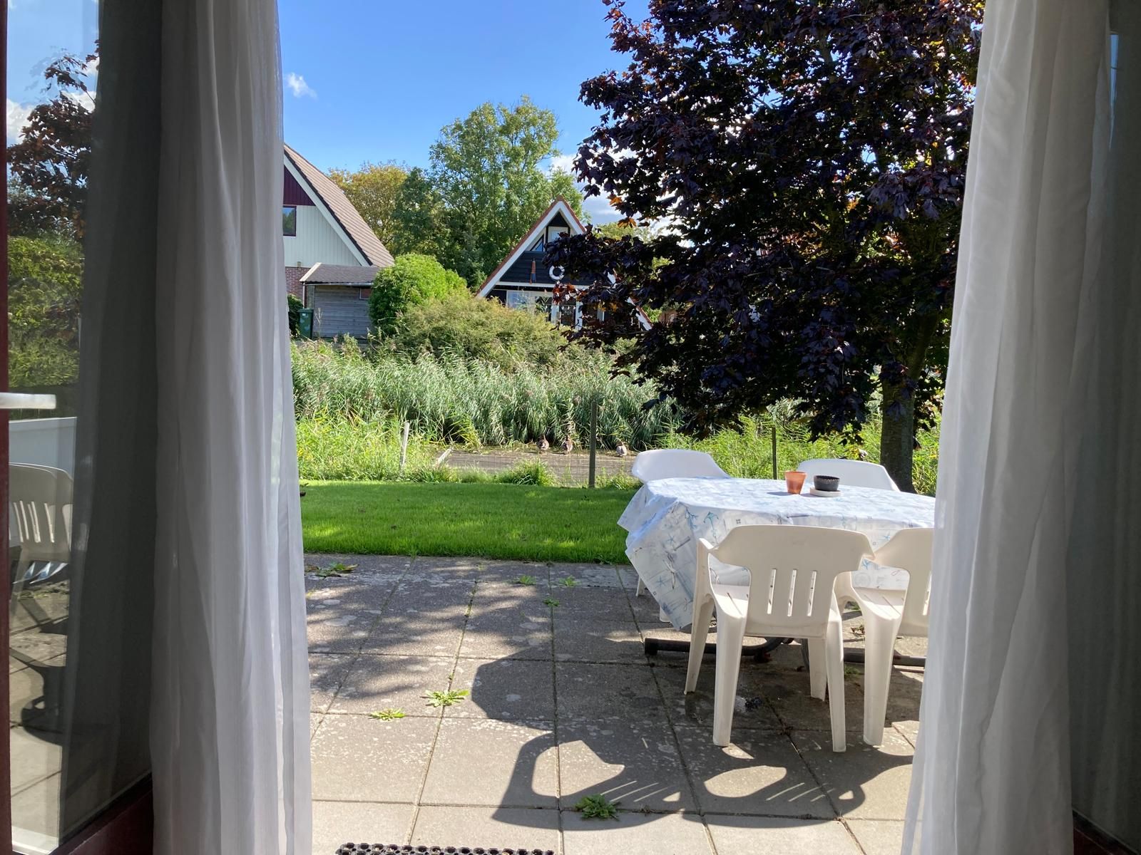 An outdoor patio area with a table and chairs, a garden view, and a building in the background.