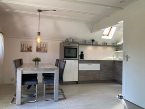 A modern kitchen with a dining area, featuring a built-in oven, a coffee machine, and a skylight. - Charming Bungalow Rental in Anjum With River Views (Anjum)