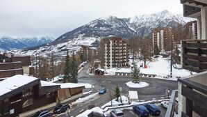 A view of a snowy mountain town with several multi-story buildings, a parking area, and a road leading to a mountain pass. - Charming studio for 4 in the heart of Les Orres 1650 (Les Orres)
