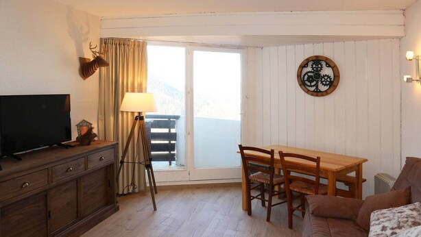 A cozy living room with a wooden TV stand, a dining table with chairs, a sofa, and a lamp. - Charming studio for 4 in the heart of Les Orres 1650 (Les Orres)