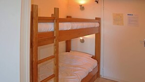 A bunk bed with two levels, a wall-mounted light, and a door with a notice on it. - Charming studio for 4 in the heart of Les Orres 1650 (Les Orres)