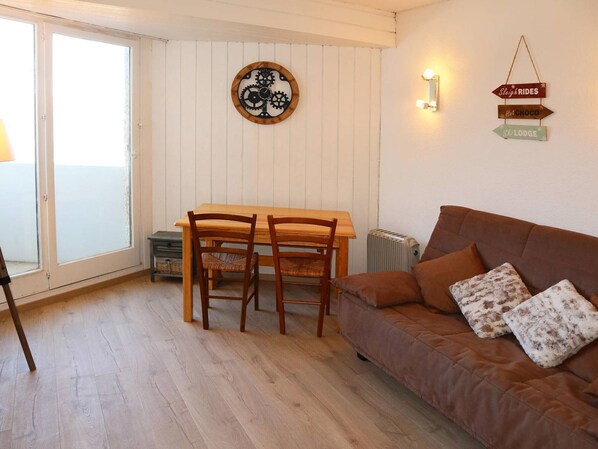 Un salon chaleureux avec une table en bois et deux chaises, un canapé marron agrémenté de coussins à motifs, une horloge murale et un panneau indiquant « Promenades en traîneau » et « Chocolat chaud ».
