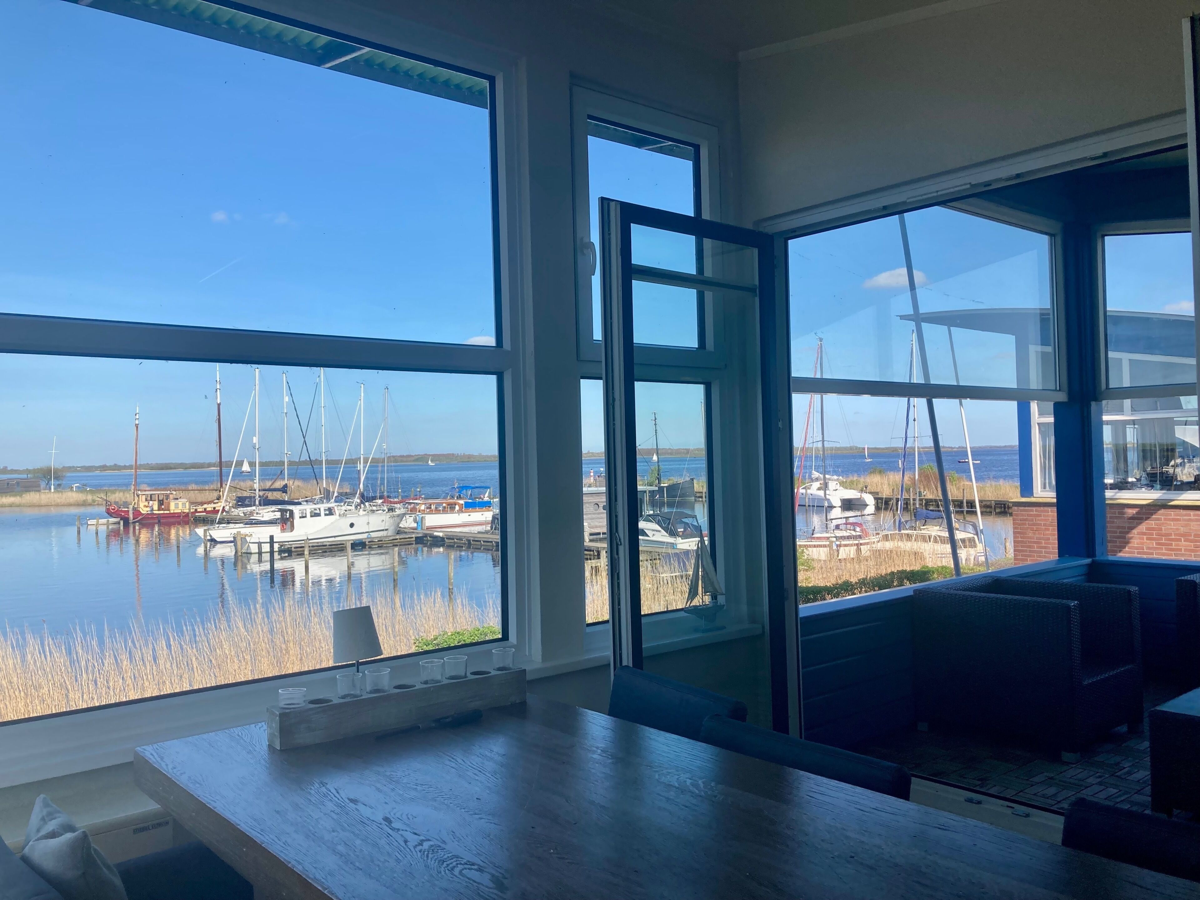 A spacious room with large windows offering a view of a marina with boats.
