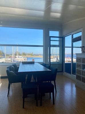 A room with a large table and chairs, a view of the marina, and a wooden floor.
