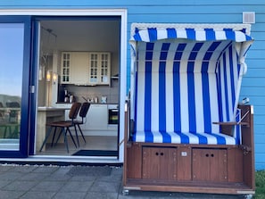 A blue building with a kitchen, a dining area, and a wooden deck with a striped awning.