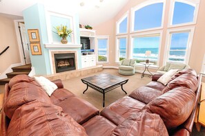 A living room with a fireplace, a large window overlooking the ocean, and a leather sofa. - OCEANFRONT, Ocean Views, Pool, Rec Rm, PI244, Ashcroft (Corolla)