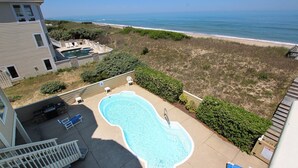 Ein Schwimmbecken mit Meerblick, umgeben von einem eingezäunten Garten mit einigen Stühlen und einer kleinen Terrasse.