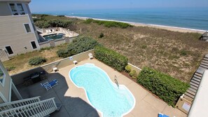 Una piscina con vistas al océano, rodeada por un patio cercado con algunas sillas y una pequeña terraza.